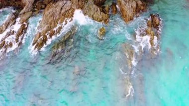4K hava aracı yukarıdan aşağıya kuş bakışı deniz mavi dalgaları kaya ve kumda kırılıyor. Deniz suyunun güzel dalgaları sahile gelir.