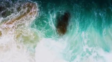 4K hava aracı yukarıdan aşağıya kuş bakışı deniz mavi dalgaları kaya ve kumda kırılıyor. Deniz suyunun güzel dalgaları sahile gelir.