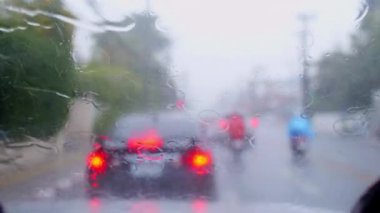 4K, ön camında yağmur damlaları olan bir trafik lambasıyla yolda duran bir arabayı kullanıyor. Ön camdan vurulmuşlar. Arabanın ön camına yağmur yağıyor..