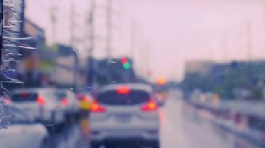 4K, ön camında yağmur damlaları olan bir trafik lambasıyla yolda duran bir arabayı kullanıyor. Ön camdan vurulmuşlar. Arabanın ön camına yağmur yağıyor..