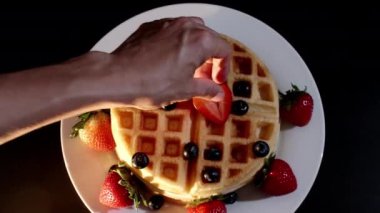 4K. Pasta şefinin eli taze pişmiş waffle 'ların üzerine yabanmersini ve ahududu koyar. Fırından taze ahududu ve böğürtlen ile süslenmiş..