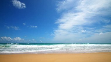 4K Mavi gökyüzü ve bulutları olan güzel tropikal plaj. Dalgaların boş plajı vurduğu tropik bir sahil. Andaman Phuket plajı Tayland. Güzel yaz gününde deniz kumu ve gökyüzü. Tatil özgürlüğü.