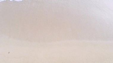 4K hava aracı yukarıdan aşağıya kuş bakışı deniz mavi dalgaları kaya ve kumda kırılıyor. Deniz suyunun güzel dalgaları sahile gelir.