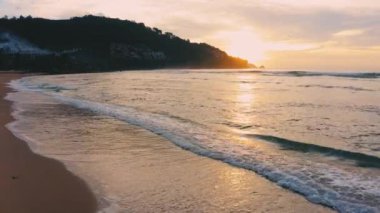 4K Günbatımı gökyüzü ile güzel tropikal plaj. Güzel Phuket plajı, Andaman Denizi yaz konseptinde ünlü bir turizm merkezidir. Denizin üzerinde günbatımı olan gerçek bir drone manzaralı tropikal plaj