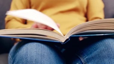 Kapalı kapılar ardında kitap çeviren kadınlar. Kadının eli kitabı tutuyor ve okurken parmaklarını sayfa boyunca hareket ettiriyor..