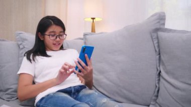 Mutlu kardeşler, oturma odasındaki kanepede oturan çocuklar, aileleriyle cep telefonunda konuşan, gülümseyen büyük kız, akıllı telefondan küçük kız kardeş videosu izleyip ailesiyle konuşuyor. Yaşam biçimi 