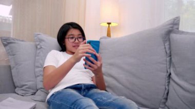 Mutlu kardeşler, oturma odasındaki kanepede oturan çocuklar, aileleriyle cep telefonunda konuşan, gülümseyen büyük kız, akıllı telefondan küçük kız kardeş videosu izleyip ailesiyle konuşuyor. Yaşam biçimi 