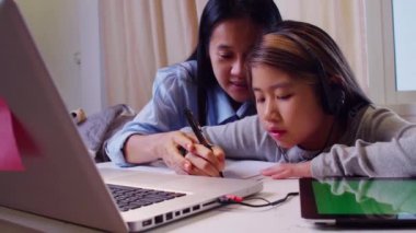 4K Asyalı küçük kız annesiyle çalışmak için dizüstü bilgisayar kullanıyor. Öğrenci çocuk ödev kitabı yazıyor. Kız evde çalışmak için bilgisayar kullanıyor. Eğitim ev okulu kavramı.