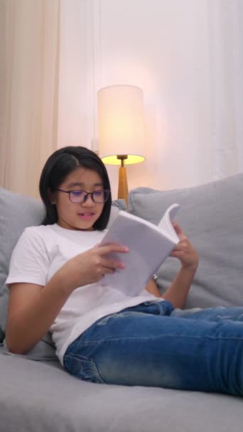 快乐的亚洲女孩坐在客厅的沙发上 用手机和父母说话 微笑的可爱女孩用智能手机和家人说话 通过因特网无线保真 — 图库视频影像