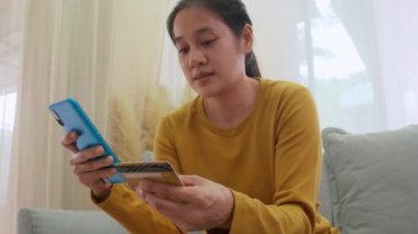 Kredi kartı tutan ve cep telefonu kullanan bir kadın. Evde çalışan kadınlar. Çevrimiçi alışveriş, e-ticaret, internet bankacılığı, harçlık, ev konseptiyle çalışmak. Çevrimiçi teknoloji alışverişi kavramı