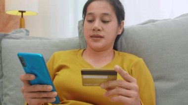 Kredi kartı tutan ve cep telefonu kullanan bir kadın. Evde çalışan kadınlar. Çevrimiçi alışveriş, e-ticaret, internet bankacılığı, harçlık, ev konseptiyle çalışmak. Çevrimiçi teknoloji alışverişi kavramı