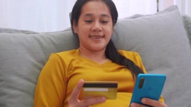 Kredi kartı tutan ve cep telefonu kullanan bir kadın. Evde çalışan kadınlar. Çevrimiçi alışveriş, e-ticaret, internet bankacılığı, harçlık, ev konseptiyle çalışmak. Çevrimiçi teknoloji alışverişi kavramı