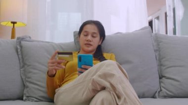 Kredi kartı tutan ve cep telefonu kullanan bir kadın. Evde çalışan kadınlar. Çevrimiçi alışveriş, e-ticaret, internet bankacılığı, harçlık, ev konseptiyle çalışmak. Çevrimiçi teknoloji alışverişi kavramı