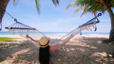 Phuket Tayland. Gün batımında sahilde hamak üzerine kitap yazan Asyalı genç bir kadın. Genç ve çekici bir kadın hamakta sallanıyor. Yaz tatili
