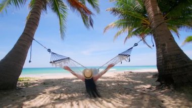 Phuket Tayland. Gün batımında sahilde hamak üzerine kitap yazan Asyalı genç bir kadın. Genç ve çekici bir kadın hamakta sallanıyor. Yaz tatili