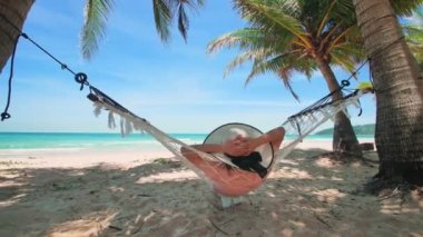 Phuket Tayland. Gün batımında sahilde hamak üzerine kitap yazan Asyalı genç bir kadın. Genç ve çekici bir kadın hamakta sallanıyor. Yaz tatili