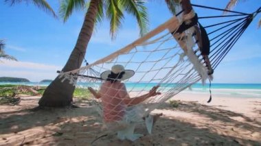 Phuket Tayland. Gün batımında sahilde hamak üzerine kitap yazan Asyalı genç bir kadın. Genç ve çekici bir kadın hamakta sallanıyor. Yaz tatili