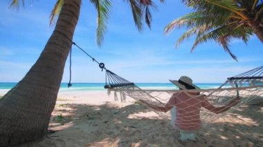 Phuket Tayland. Gün batımında sahilde hamak üzerine kitap yazan Asyalı genç bir kadın. Genç ve çekici bir kadın hamakta sallanıyor. Yaz tatili