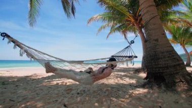 Phuket Tayland. Gün batımında sahilde hamak üzerine kitap yazan Asyalı genç bir kadın. Genç ve çekici bir kadın hamakta sallanıyor. Yaz tatili