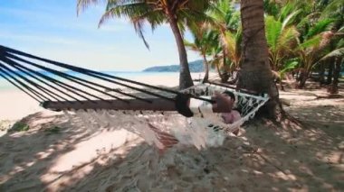 Phuket Tayland. Gün batımında sahilde hamak üzerine kitap yazan Asyalı genç bir kadın. Genç ve çekici bir kadın hamakta sallanıyor. Yaz tatili