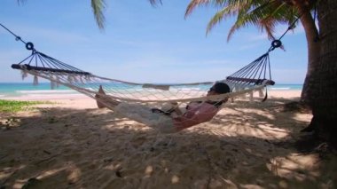 Phuket Tayland. Gün batımında sahilde hamak üzerine kitap yazan Asyalı genç bir kadın. Genç ve çekici bir kadın hamakta sallanıyor. Yaz tatili