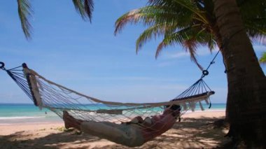 Phuket Tayland. Gün batımında sahilde hamak üzerine kitap yazan Asyalı genç bir kadın. Genç ve çekici bir kadın hamakta sallanıyor. Yaz tatili