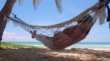 Phuket Tayland. Gün batımında sahilde hamak üzerine kitap yazan Asyalı genç bir kadın. Genç ve çekici bir kadın hamakta sallanıyor. Yaz tatili