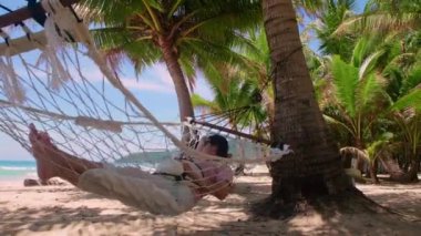 Phuket Tayland. Gün batımında sahilde hamak üzerine kitap yazan Asyalı genç bir kadın. Genç ve çekici bir kadın hamakta sallanıyor. Yaz tatili