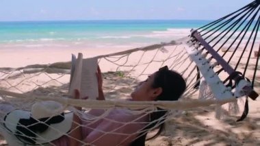 Phuket Tayland. Gün batımında sahilde hamak üzerine kitap yazan Asyalı genç bir kadın. Genç ve çekici bir kadın hamakta sallanıyor. Yaz tatili