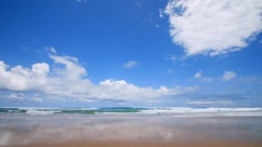 4K Mavi gökyüzü ve bulutları olan güzel tropikal plaj. Dalgaların boş plajı vurduğu tropik bir sahil. Andaman Phuket plajı Tayland. Güzel yaz gününde deniz kumu ve gökyüzü. Tatil özgürlüğü.