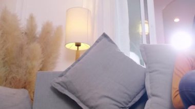 Oturma odasında kitap okuyan genç bir kadın. Kadınlar evdeki kanepede oturup kitap okuyorlar. Kadın hafta sonları boş zamanlarında rahat bir kanepede rahatlar.