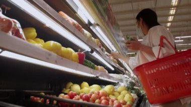 Yeni normal sosyal mesafeli konsept Asyalı kadın koruyucu yüz maskesi takıyor ve marketten meyve seçiyor. Coronavirüs sonrası markette meyve satan kadınlar, covid-19 salgını