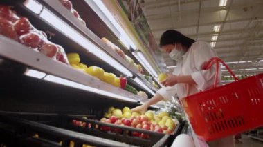 Yeni normal sosyal mesafeli konsept Asyalı kadın koruyucu yüz maskesi takıyor ve marketten meyve seçiyor. Coronavirüs sonrası markette meyve satan kadınlar, covid-19 salgını