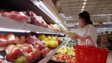 Yeni normal sosyal mesafeli konsept Asyalı kadın koruyucu yüz maskesi takıyor ve marketten meyve seçiyor. Coronavirüs sonrası markette meyve satan kadınlar, covid-19 salgını