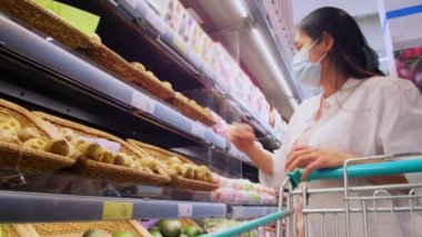 Yeni normal sosyal mesafeli konsept Asyalı kadın koruyucu yüz maskesi takıyor ve marketten meyve seçiyor. Coronavirüs sonrası markette meyve satan kadınlar, covid-19 salgını