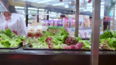 Koruyucu yüz maskesi takan yeni normal Asyalı kadınlar maşa kullanıyor. Süpermarketteki salata barından sebze alıyorlar.