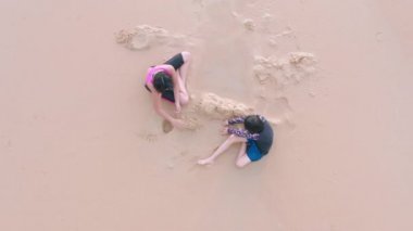 4K hava aracı üst görüntüsü. İki mutlu küçük kız sahilde birlikte kum oynuyor. Aileden iki kız sahilde dinleniyor. Hayat tarzı seyahat tatili aile kavramı.
