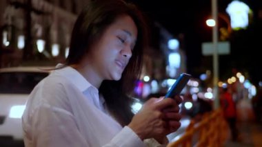 Gece vakti akıllı telefon kullanan Asyalı gülümseyen kadın. Kadınlar şehirde yürürken telefonda sohbet ediyorlar. Sokakta tek başına dolaşan bir kadın, gece yolundaki arkadaşıyla akıllı telefon iletişimi kuruyor. Yaşam tarzı kavramı