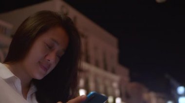 Gece vakti akıllı telefon kullanan Asyalı gülümseyen kadın. Kadınlar şehirde yürürken telefonda sohbet ediyorlar. Sokakta tek başına dolaşan bir kadın, gece yolundaki arkadaşıyla akıllı telefon iletişimi kuruyor. Yaşam tarzı kavramı