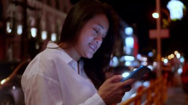 Gece vakti akıllı telefon kullanan Asyalı gülümseyen kadın. Kadınlar şehirde yürürken telefonda sohbet ediyorlar. Sokakta tek başına dolaşan bir kadın, gece yolundaki arkadaşıyla akıllı telefon iletişimi kuruyor. Yaşam tarzı kavramı