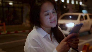 Gece vakti akıllı telefon kullanan Asyalı gülümseyen kadın. Kadınlar şehirde yürürken telefonda sohbet ediyorlar. Sokakta tek başına dolaşan bir kadın, gece yolundaki arkadaşıyla akıllı telefon iletişimi kuruyor. Yaşam tarzı kavramı