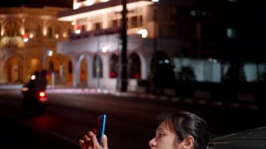 Gece vakti akıllı telefon kullanan Asyalı gülümseyen kadın. Kadınlar şehirde yürürken telefonda sohbet ediyorlar. Sokakta tek başına dolaşan bir kadın, gece yolundaki arkadaşıyla akıllı telefon iletişimi kuruyor. Yaşam tarzı kavramı