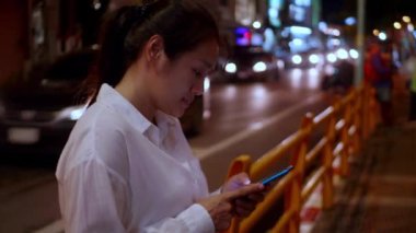 Gece vakti akıllı telefon kullanan Asyalı gülümseyen kadın. Kadınlar şehirde yürürken telefonda sohbet ediyorlar. Sokakta tek başına dolaşan bir kadın, gece yolundaki arkadaşıyla akıllı telefon iletişimi kuruyor. Yaşam tarzı kavramı