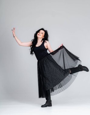 Siyah elbiseli genç esmer kadın gri arka planda poz veriyor. Stüdyoda siyah elbiseli manken..