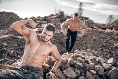 Çıplak vücutlu kaslı adamlar gergin ellerle poz veriyorlar. Açık hava fotoğrafı. Siyah pantolonlu yakışıklı bir adamın portresi.