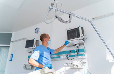 Mavi elbiseli ve maskeli doktor üzerinde sağlık parametreleri olan ekrana bakıyor. Tıbbi oda. İlk yardım. Canlandırma