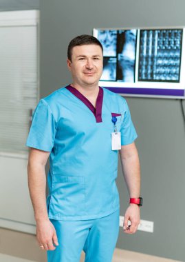 Üniforma konusunda yakışıklı bir tıp uzmanı. Modern hastanede mavi üniformalı genç adam kameraya poz veriyor..