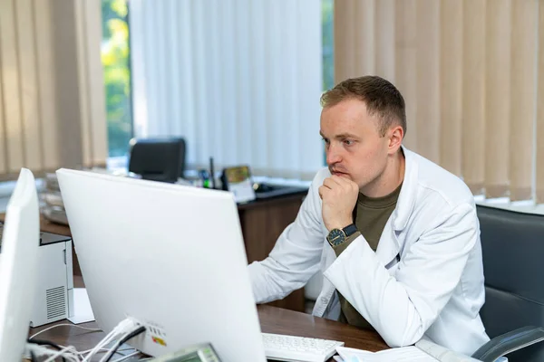 Przystojny Lekarz Mundurze Pracujący Komputerem Atrakcyjny Młody Specjalista Medyczny Siedzi — Zdjęcie stockowe