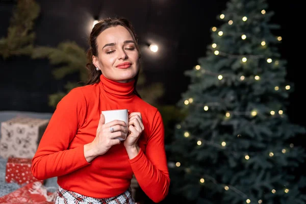 스웨터를 여자가 있습니다 크리스마스 근처에서 크리스마스 트리로 둘러싸인 마시고 — 스톡 사진