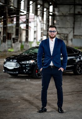 Siyah elbiseli ve güneş gözlüklü vahşi genç adam kameraya bakıyor. Terk edilmiş, deponun bulanık arka planı